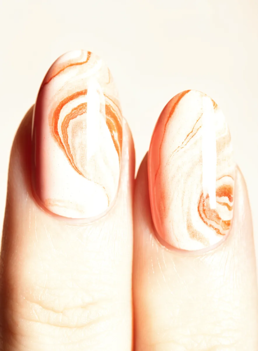 Close-up of fingertips with coral and cream marble nail art