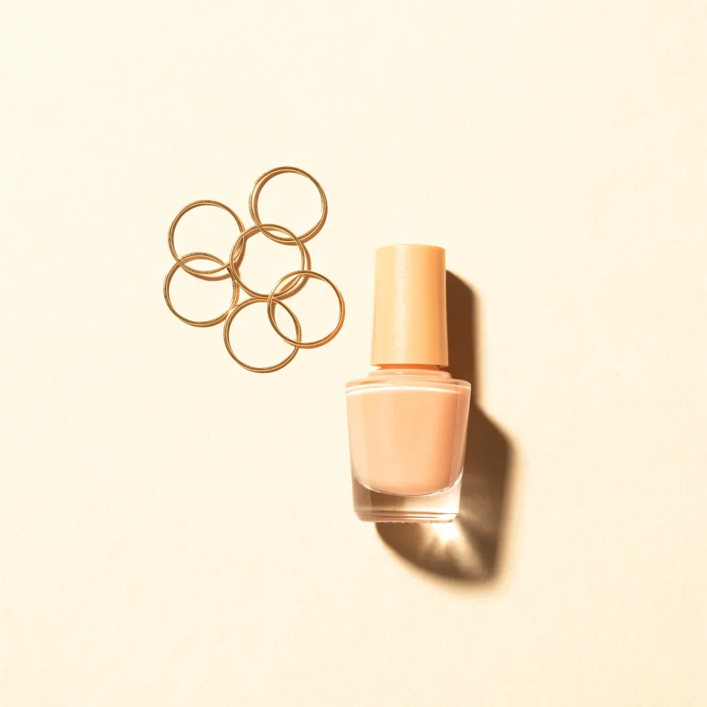 Overhead still life of stacked gold rings beside a peach nail polish bottle